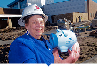 Meals on Wheels of Tarrant County CEO holds up Capital Impact Mascot PennyWise in front of construction site